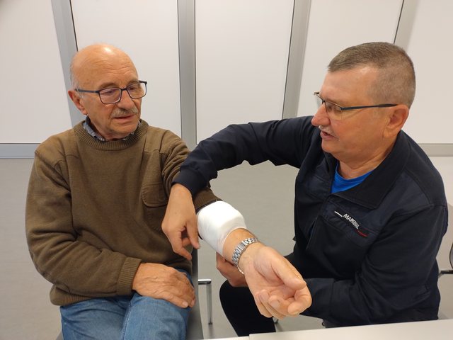 Instruktorka pokazuje seniorowi zasady opatrywania ręki podczas szkolenia